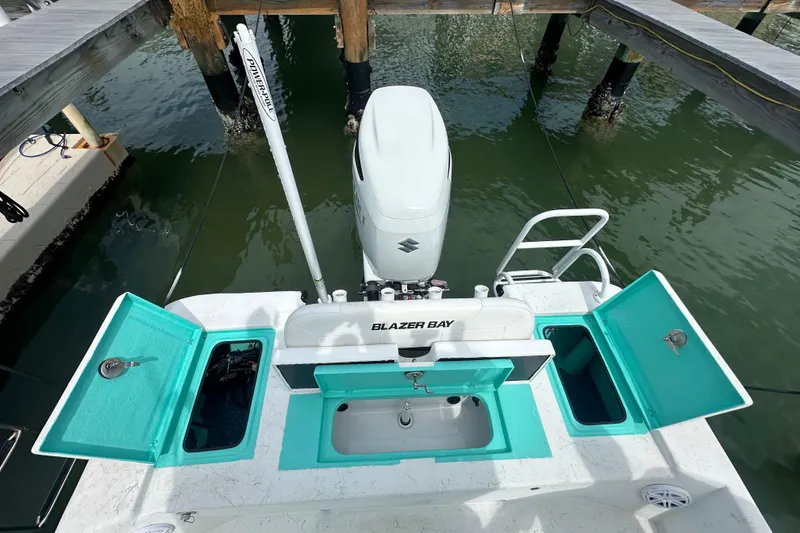 Slide: The Image of 2023 Blazer Bay 2400 boat with open storage compartments and motor, docked on calm water. - 5