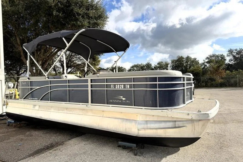 Slide: The Image of 2023 Bennington 22SSR pontoon boat with canopy, parked outdoors under a cloudy sky. - 2