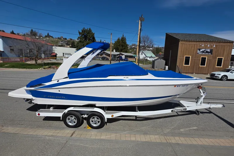 Slide: The Image of 2013 Regal 2500 Bowrider boat on trailer, blue and white design, parked on street. - 6