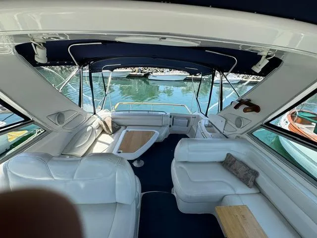 Slide: The Image of 1998 Bayliner 4085 Avanti Sunbridge interior with white seating and blue canopy on water. - 2