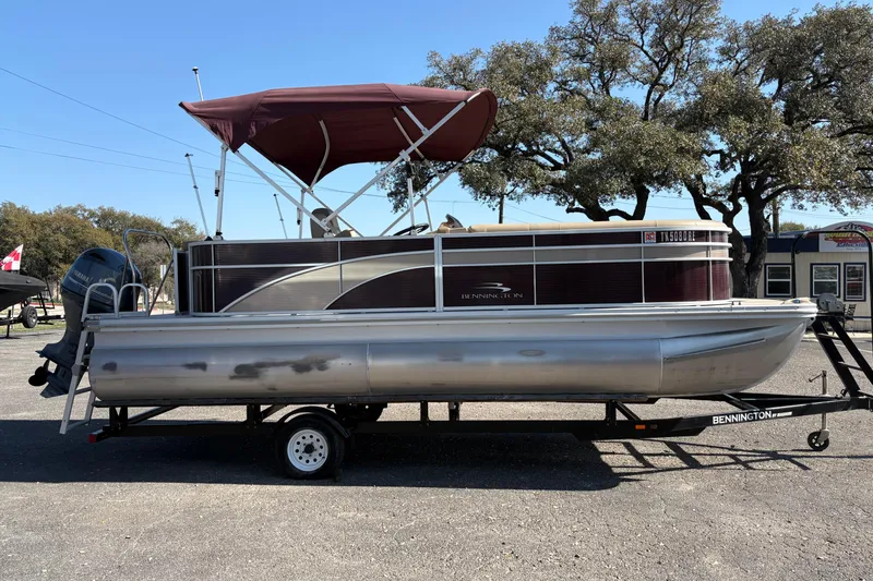 Slide: The Image of 2016 Bennington 21 SLX pontoon boat on trailer with maroon canopy, parked outdoors. - 4
