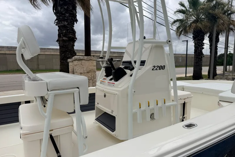 Slide: The Image of 2026 Pathfinder 2200 TRS boat interior with seating and console, parked near palm trees. - 10