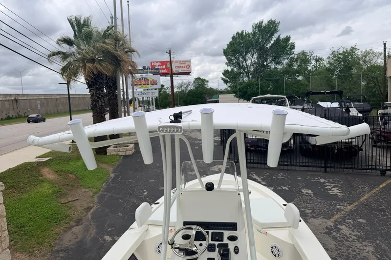 Slide: The Image of 2026 Pathfinder 2200 TRS boat with T-top and rod holders, parked near palm trees. - 16