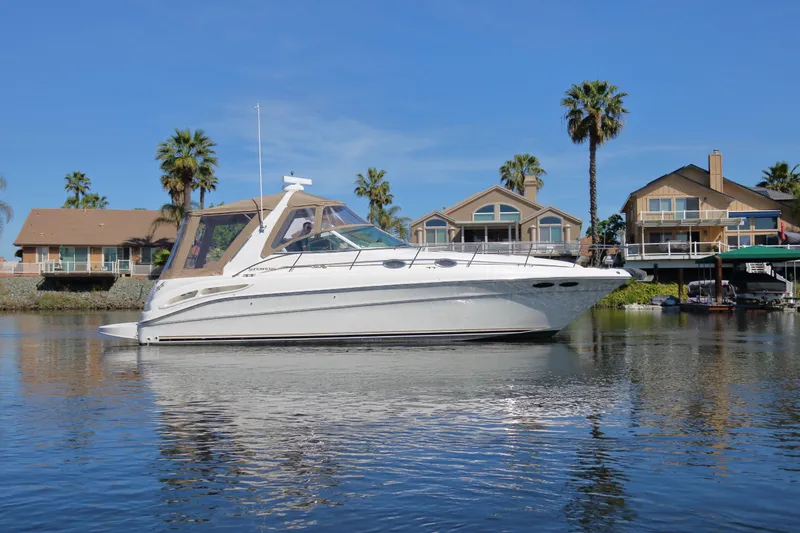 The Image of 2000 Sea Ray 340 Sundancer yacht on calm water, with waterfront homes and palm trees in the background. - 0