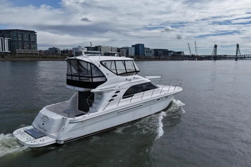 The Image of 1999 Sea Ray 560 Sedan Bridge yacht cruising on a river with cityscape background. - 0