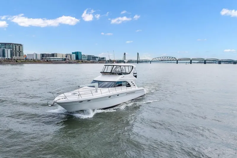 Slide: The Image of 1999 Sea Ray 560 Sedan Bridge yacht cruising on a river with cityscape and bridge background. - 11