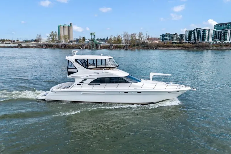Slide: The Image of 1999 Sea Ray 560 Sedan Bridge yacht cruising on a river with cityscape background. - 13
