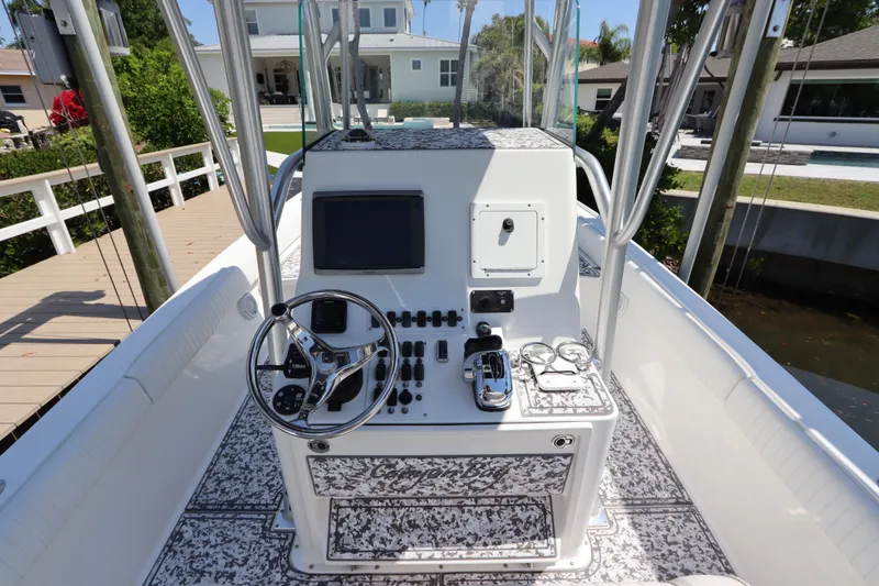 Slide: The Image of 2014 Canyon Bay 2400 boat console with steering wheel and controls, docked near waterfront homes. - 17