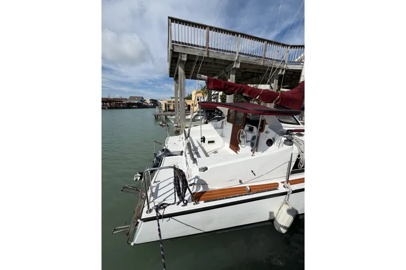 Slide: The Image of 1989 Gemini 3000 sailboat docked, featuring maroon sails and wooden accents under a clear sky. - 3
