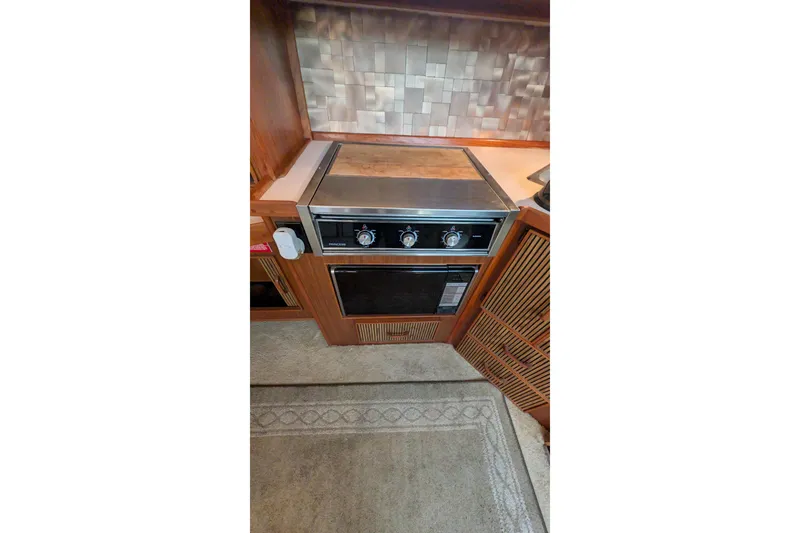 Slide: The Image of 1987 Sea Ray 390 Express Cruiser kitchen with stove and oven, featuring wood cabinetry. - 25