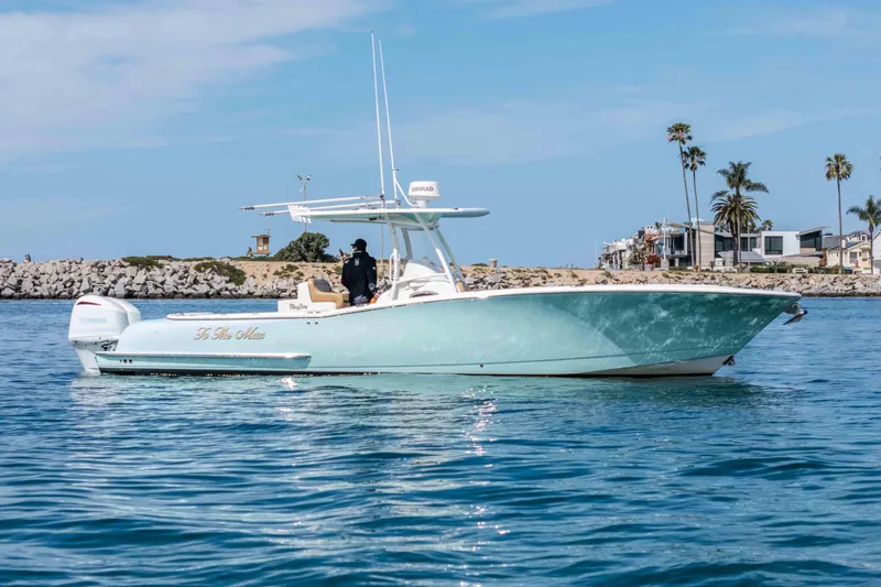 Slide: The Image of 2015 Mag Bay 33 CC boat cruising near a rocky shoreline with palm trees. - 1