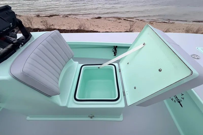 Slide: The Image of 2025 Hell's Bay Professional boat with open storage compartment and cushioned seat by the shore. - 44