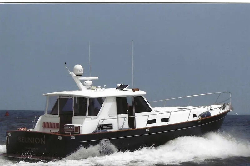 Slide: The Image of Legacy Yachts 52 Express 2002 boat named "Reunion" on water near forested shoreline. - 3