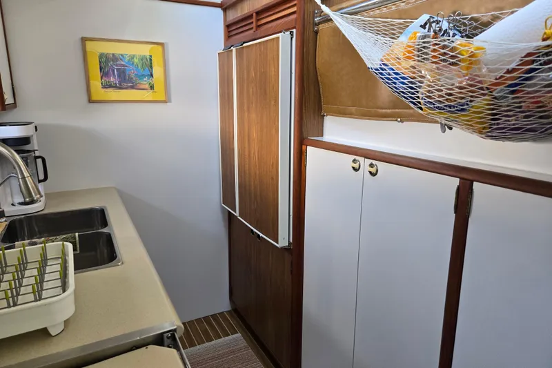Slide: The Image of Compact kitchen in a 2003 Endeavour Trawler Cat 44, featuring wooden cabinets and a netted storage area. - 49