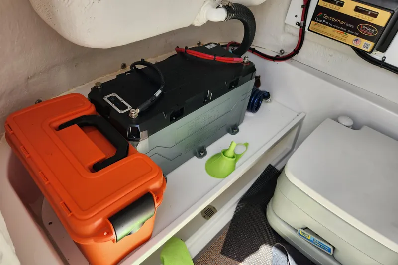 Slide: The Image of 2024 Sportsman Open 232 Center Console storage area with battery, orange case, and portable toilet. - 38