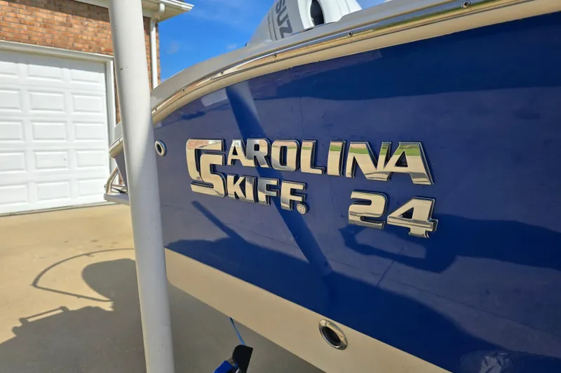 Slide: The Image of 2024 Carolina Skiff 24 Ultra Elite boat, blue hull, parked near a garage. - 7