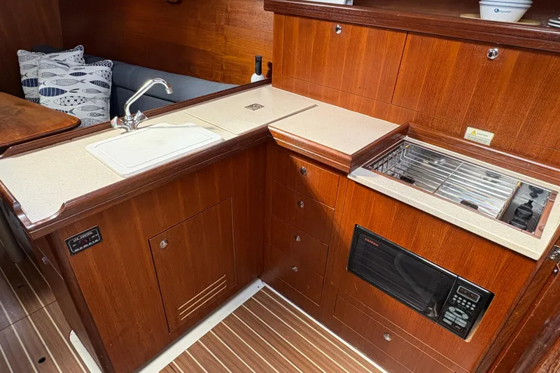 Slide: The Image of 2006 Hunter 31 yacht interior kitchen with wood cabinetry, sink, stove, and microwave. - 10