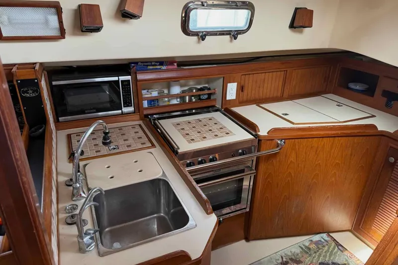 Slide: The Image of 1998 Island Packet 40 yacht kitchen with sink, stove, and microwave in a wooden interior. - 4