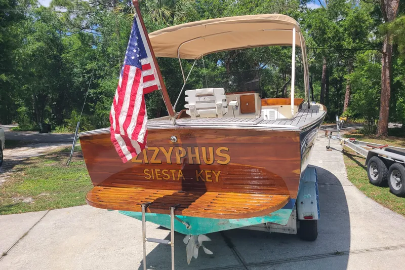 Slide: The Image of 1964 Holmes 25 Cuddy boat with American flag, named "Zizyphus," on trailer in sunny setting. - 2