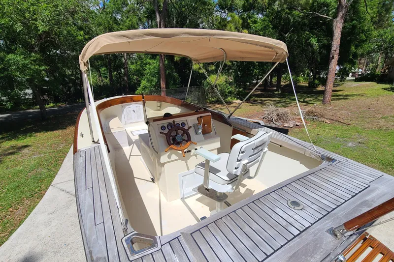 Slide: The Image of 1964 Holmes 25 Cuddy boat with canopy, wooden deck, and steering wheel in a lush setting. - 22
