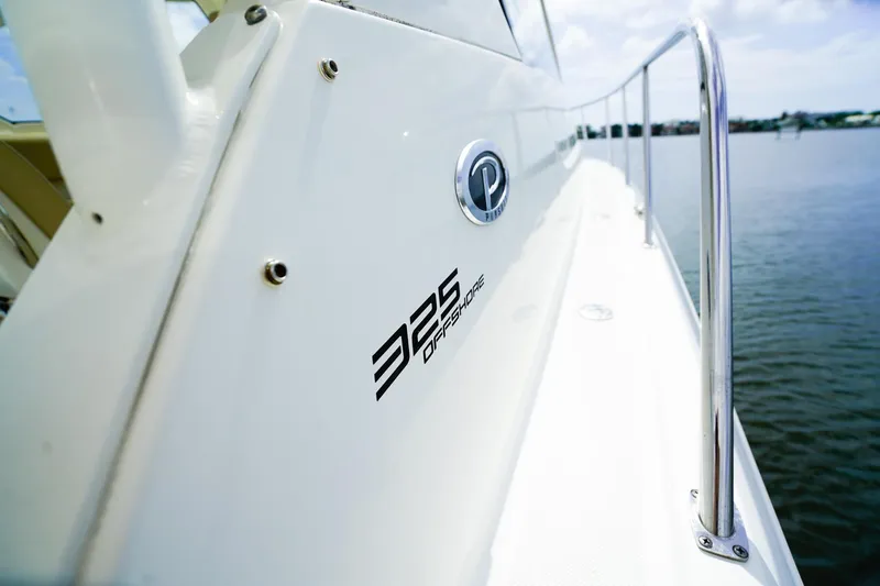 Slide: The Image of 2020 Pursuit OS 325 Offshore boat side view with logo, railing, and water backdrop. - 34