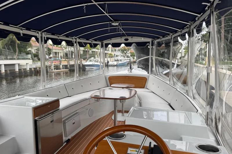 Slide: The Image of 2023 Duffy Bay Island 22 boat interior with seating, table, and canopy on a calm waterway. - 12