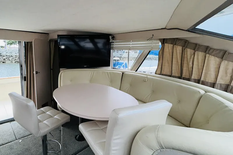 Slide: The Image of Interior of 1988 Sea Ray 265 Sedan Bridge with round table, TV, and cushioned seating. - 8