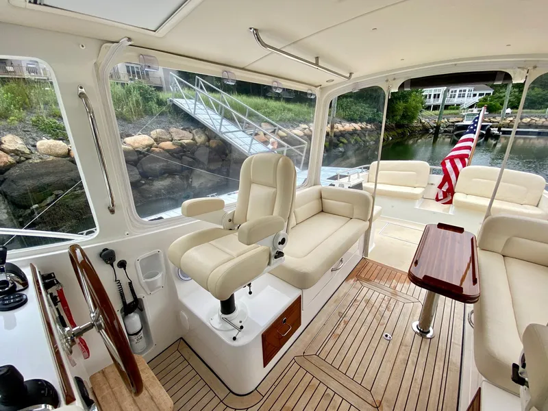 Slide: The Image of 2013 MJM 36z Downeast boat interior with plush seating and wooden accents, docked by a scenic shoreline. - 18