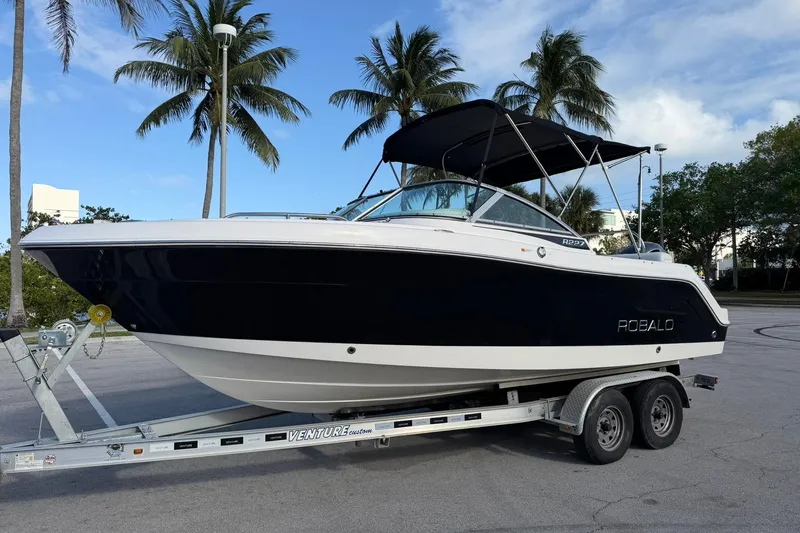 The Image of 2016 Robalo R227 Dual Console boat on trailer, parked under palm trees. - 1