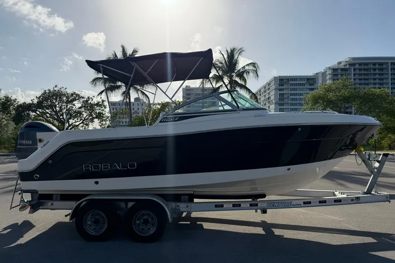 Slide: The Image of 2016 Robalo R227 Dual Console boat on trailer, parked outdoors with palm trees and buildings in background. - 6