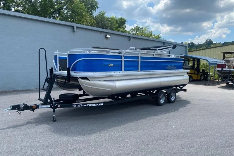 Slide: The Image of 2026 Sun Tracker Fishin' Barge 20 DLX pontoon boat on trailer, parked outdoors. - 105