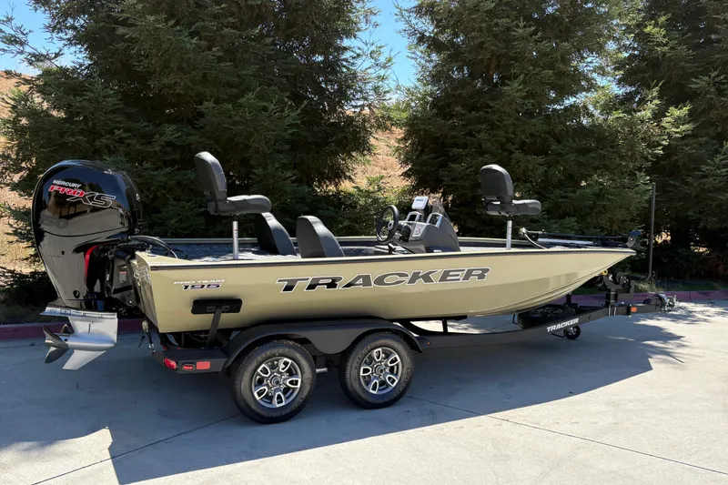 Slide: The Image of 2026 Tracker Pro Team 195 boat on trailer, parked outdoors near trees. - 2