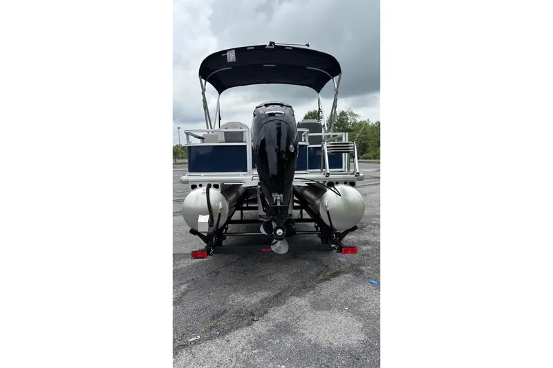 Slide: The Image of 2026 Sun Tracker Bass Buggy 18 DLX pontoon boat, rear view with motor, parked outdoors. - 3