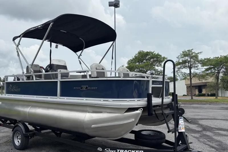 Slide: The Image of 2026 Sun Tracker Bass Buggy 18 DLX pontoon boat on trailer, parked outdoors. - 4