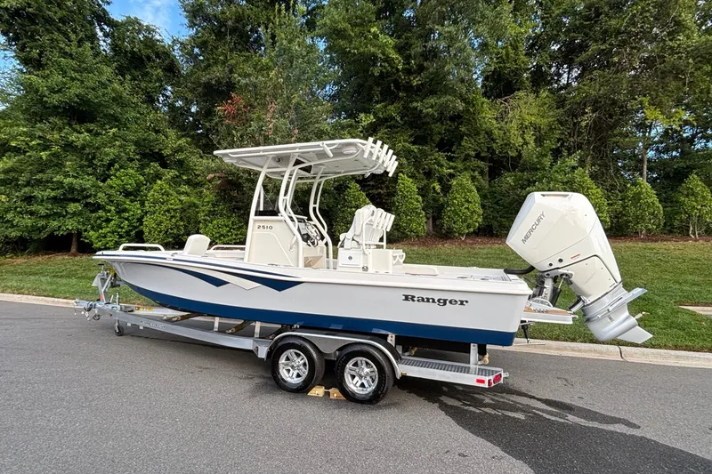 Slide: The Image of 2026 Ranger 2510 Bay boat on trailer, parked on road with lush green background. - 3