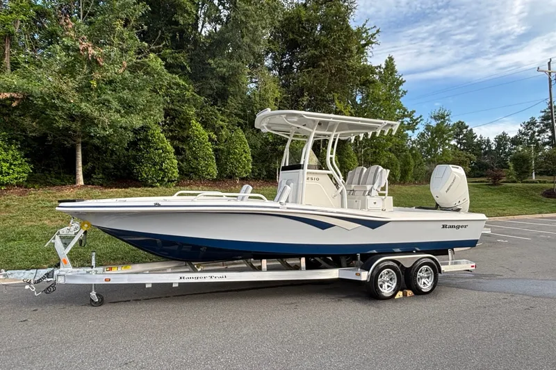 Slide: The Image of 2026 Ranger 2510 Bay boat on trailer, parked outdoors with lush greenery background. - 1