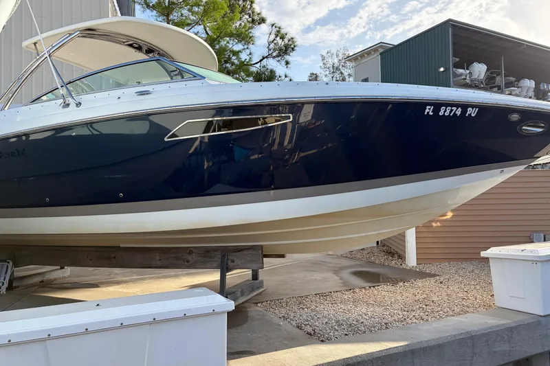 The Image of 2015 Cobalt 336 boat on dry dock, blue and white hull, sunny day. - 0