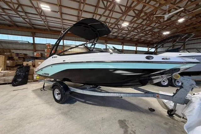 The Image of 2026 Yamaha Boats AR195 in a warehouse, sleek design on a trailer. - 0