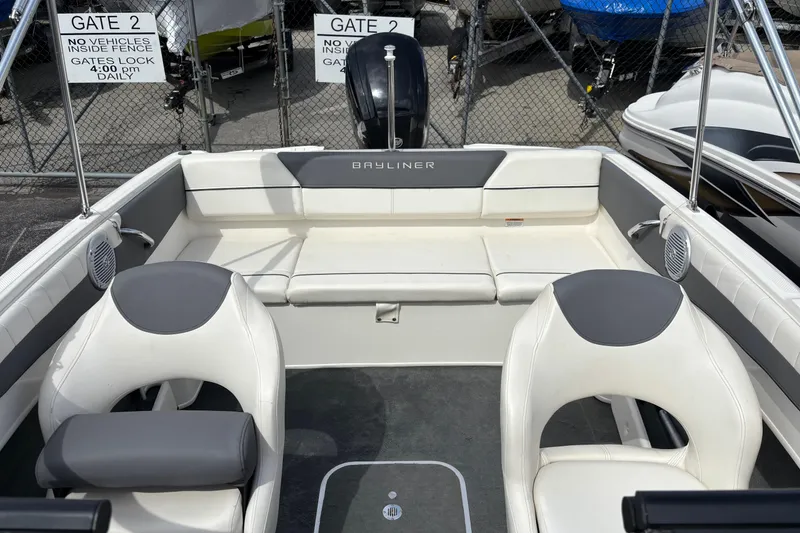 Slide: The Image of 2018 Bayliner 180 Bowrider interior with seating and steering wheel, parked near gated area. - 11