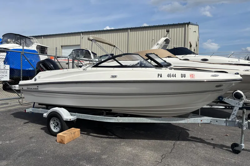 Slide: The Image of 2018 Bayliner 180 Bowrider boat on trailer, parked outdoors near other boats. - 5