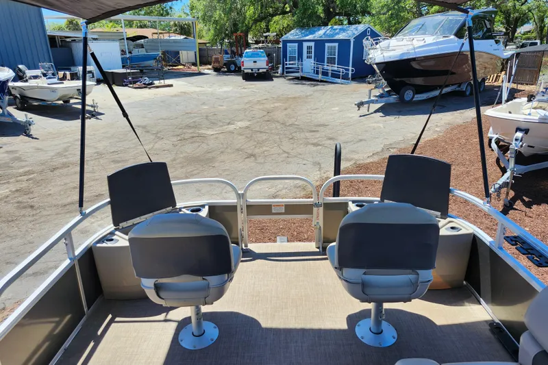 Slide: The Image of 2023 Sun Tracker Fishin' Barge 22 XP3 interior with seating, parked in a boatyard. - 21
