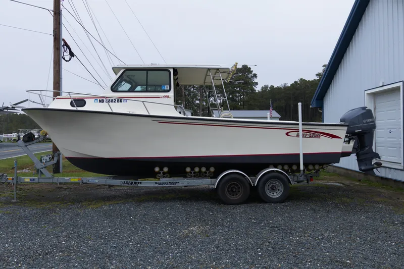 The Image of 2000 May-Craft 2550 Cabin boat on trailer, parked near a building. - 1