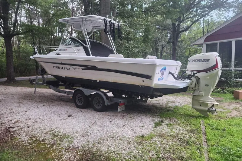 Slide: The Image of 1999 Pro-Line 241 Walkaround boat on trailer with Evinrude outboard motor in wooded area. - 3
