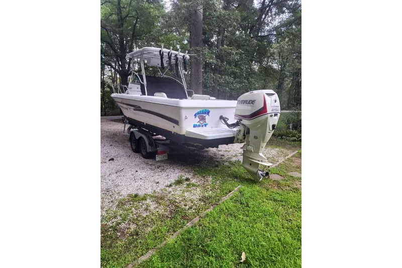 Slide: The Image of 1999 Pro-Line 241 Walkaround boat with Evinrude engine, parked on a gravel driveway. - 4