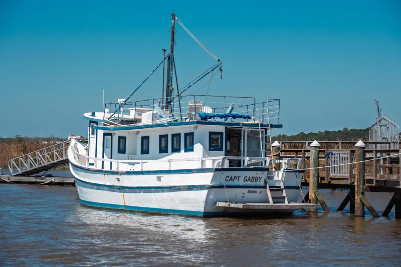 Slide: The Image of 1977 Saint Augustine 43 Trawler docked, named "Capt Gabby," in a serene marina setting. - 4