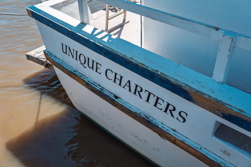 Slide: The Image of 1977 Saint Augustine Trawler 43 with "Unique Charters" sign, docked on calm water. - 9