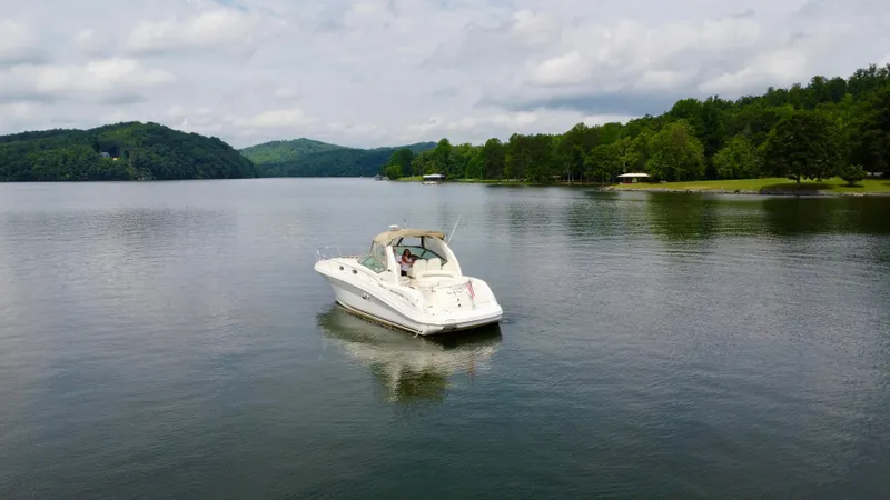 Slide: The Image of 2003 Sea Ray 340 Sundancer boat on a serene lake with lush green surroundings. - 5