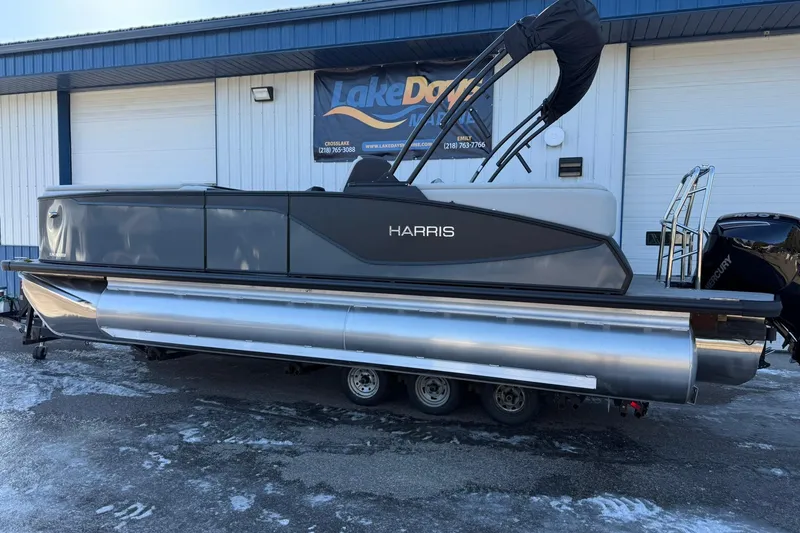 Slide: The Image of 2026 Harris Sunliner 230 pontoon boat on trailer, parked outside a marine dealership. - 14