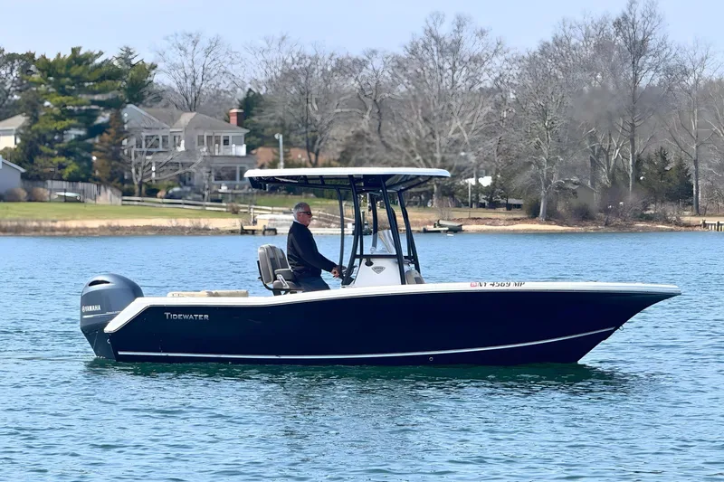 Slide: The Image of 2019 Tidewater 220 LXF boat cruising on a calm lake with scenic background. - 2