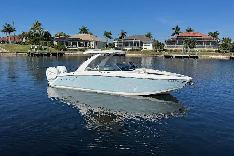 Slide: The Image of 2018 Cobalt 30SC boat on calm water, with waterfront homes and palm trees in the background. - 2